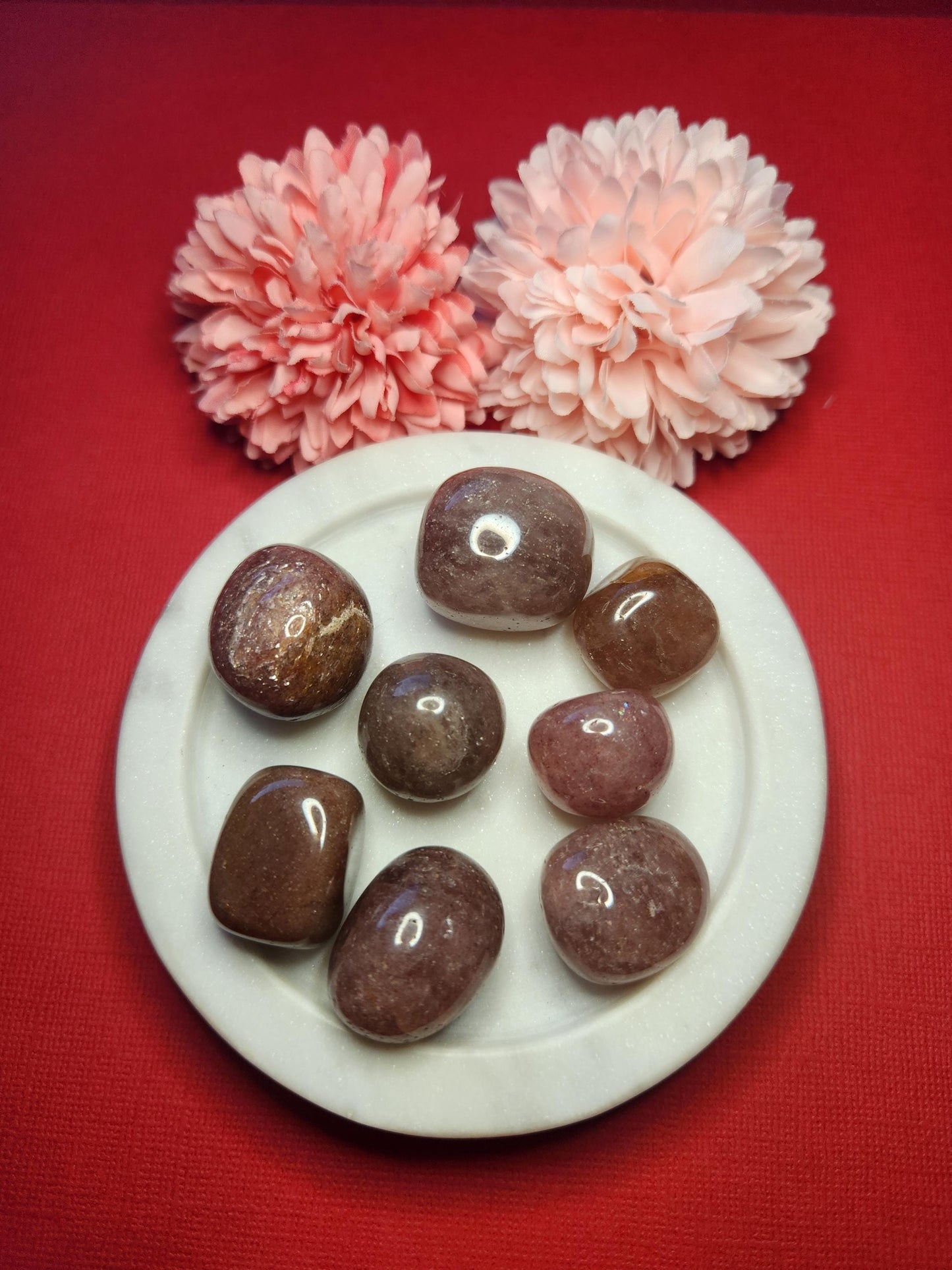 Strawberry Quartz tumbles displayed on a vibrant red background, showcasing their soft pink hues and polished surfaces. These tumbled gemstones are known for their love energy and heart chakra healing properties. Perfect for crystal collectors, meditation, and spiritual practices. The rich red backdrop enhances the warm, gentle energy of the stones, making them ideal for self-care, gifting, and energy work.
