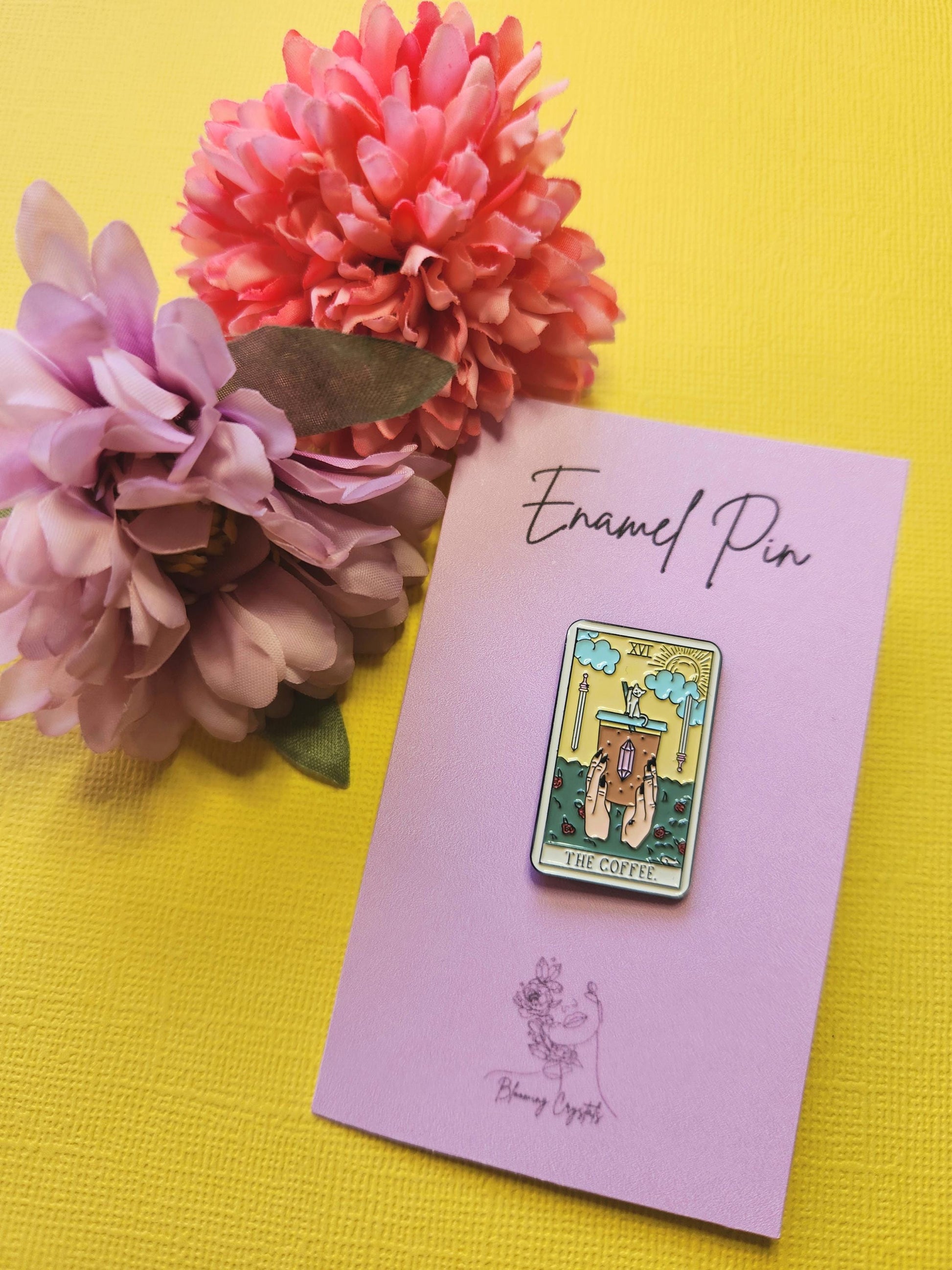 Enamel pin designed as a traditional tarot card featuring an iced coffee illustration, styled with two flowers on a bright yellow backdrop — perfect for coffee lovers, tarot fans, and enamel pin collectors.