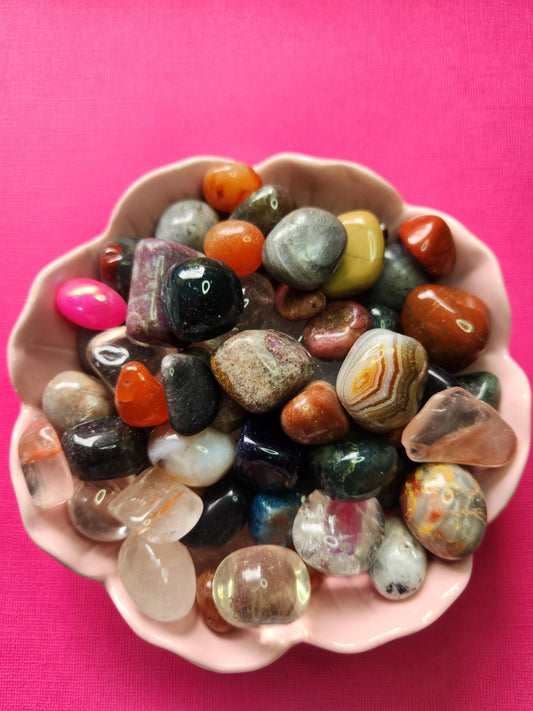 Flatlay photo of colourful crystal tumbles confetti displayed in a pink flower-shaped bowl against a soft pink backdrop, featuring mixed gemstone chips and mini tumbles perfect for crystal crafting, spiritual healing, intention setting, altar decor, crystal collections, and witchy gift ideas. High-quality close-up image showing polished crystal tumbles with vibrant colours for Etsy product listing SEO, metaphysical shop marketing, and gemstone accessory inspiration
