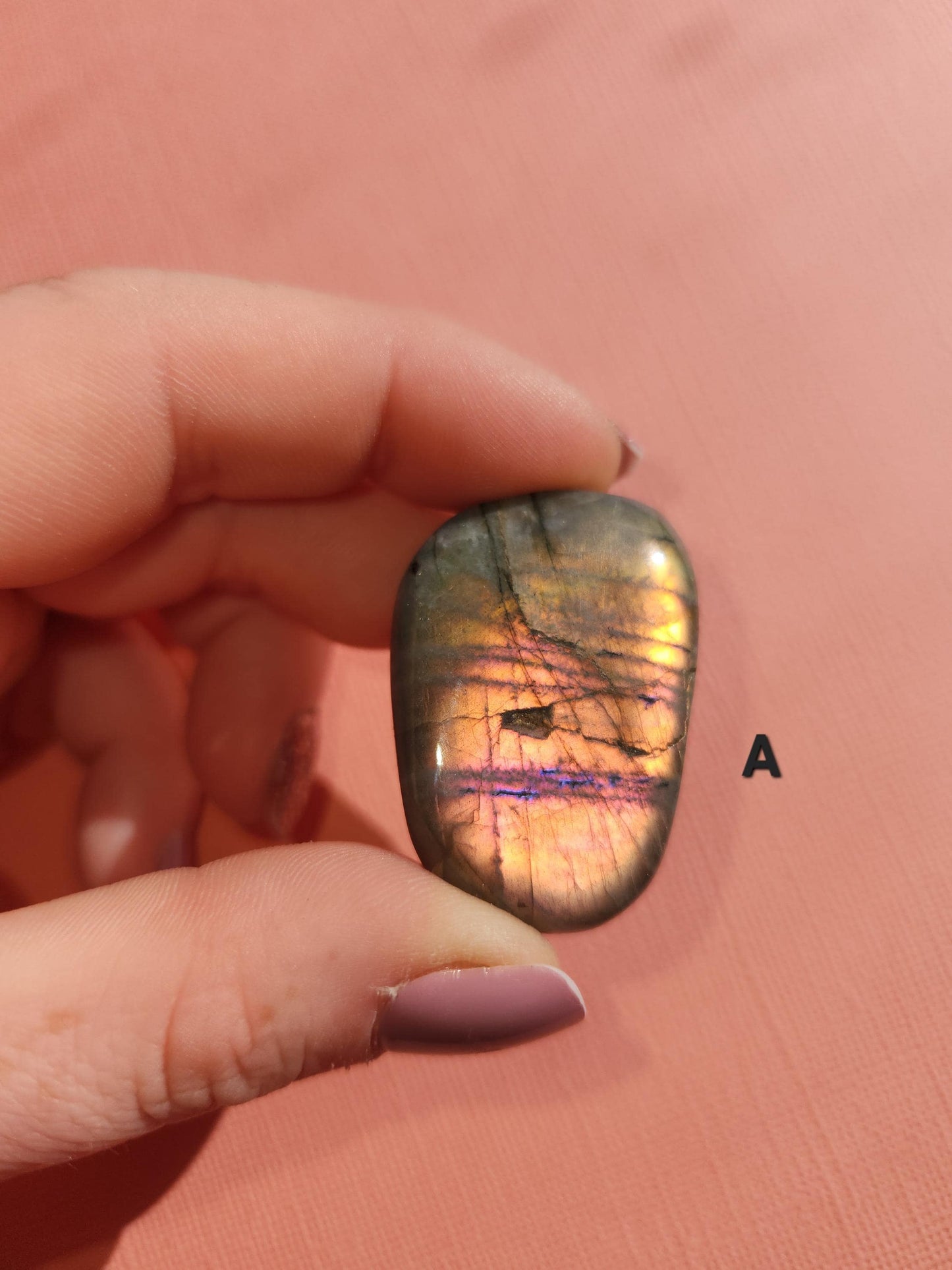 Close-up of a polished Labradorite palm stone showing vibrant pink flash on a pink background. This natural healing crystal is ideal for intuition, spiritual protection, and emotional balance. Labradorite is a popular choice for chakra work, especially the third eye and crown chakras. Perfect for energy healing, meditation, crystal grids, or gifting to spiritual wellness lovers.